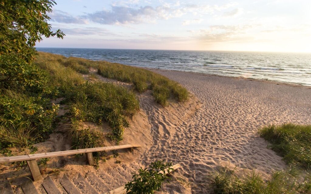  A photo of a sandy beach with a wooden bench at the top of a dune, which can be used to represent the search query 'Budgeting for a vacation'.